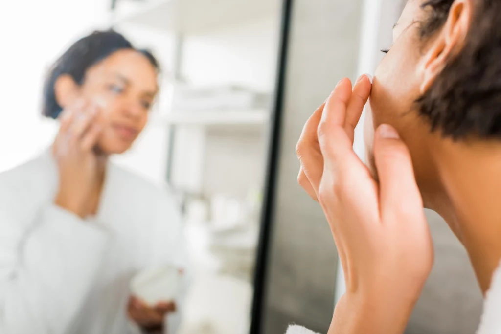 woman applying moisturizer in front of mirror 2026 03 12 23 52 03 utc